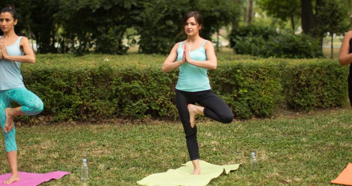 three women performing tree pose in outdoor yoga class