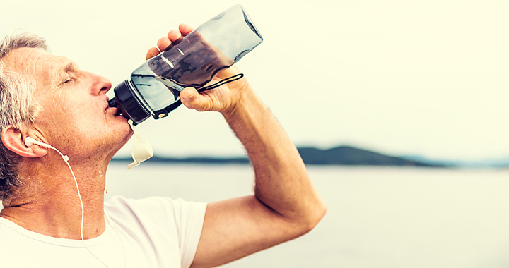 man drinks from water bottle on a beach _ how to protect your heart from the heat