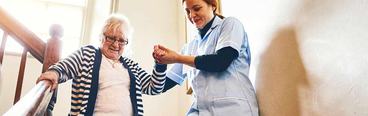 female health care worker helping female patient down stairs after joint replacement