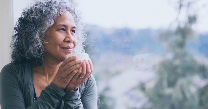 woman practicing mindfulness while holding a white mug looking out the window