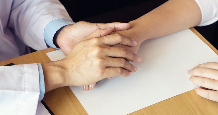 Health care provider holding a patient's hand on wooden table that has a paper on it