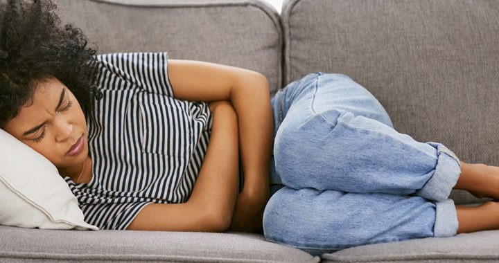 Woman lying on couch with both arms wrapped around abdomen - IBS Triggers