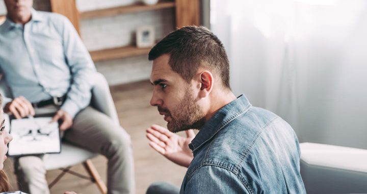 Couple sitting on couch with intense faces looks to be arguiing in front of therapist during marriage counseling