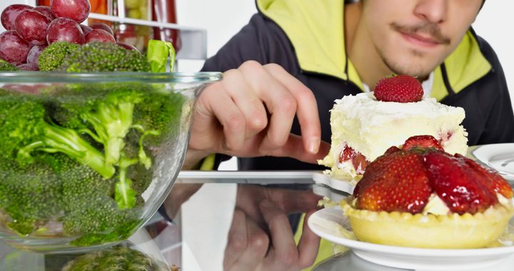 Young man looking at desserts in refrigerator and ignoring vegetables - elimination diet