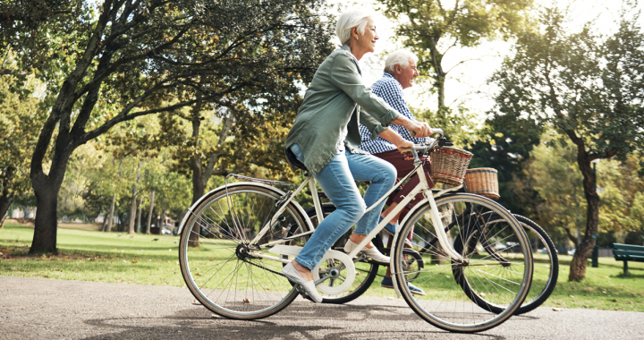 An elderly man and woman take a bike ride down a tree covered path