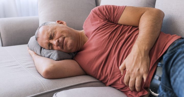 A middle-aged man who has IBS lays on a couch and clutches his stomach in pain