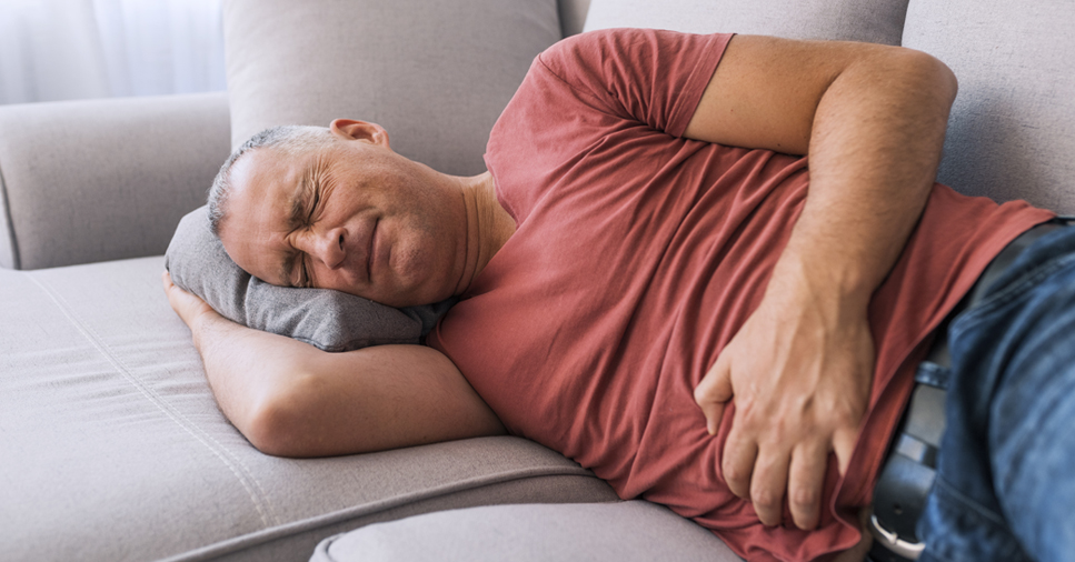 A middle-aged man who has IBS lays on a couch and clutches his stomach in pain