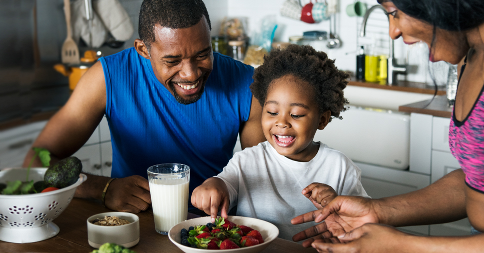 Two parents and their son eat breakfast at a table together to practice healthy habits