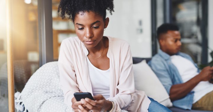 A woman on her phone browsing social media sits facing away from her boyfriend who is also on his phone