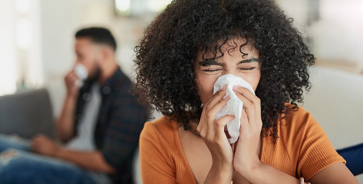 A woman sneezing into a tissue while at home.