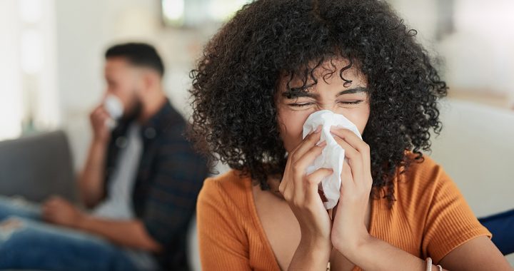 A woman sneezing into a tissue while at home.