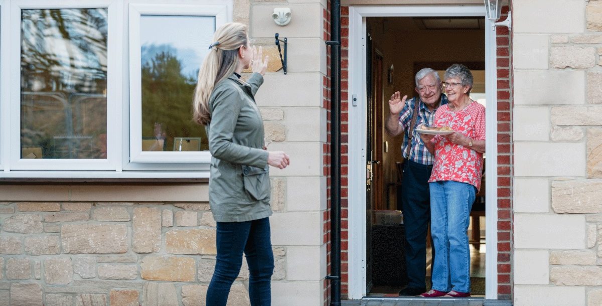 Woman waving to loved ones from outside their home during COVID-19.