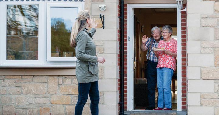 Woman waving to loved ones from outside their home during COVID-19.