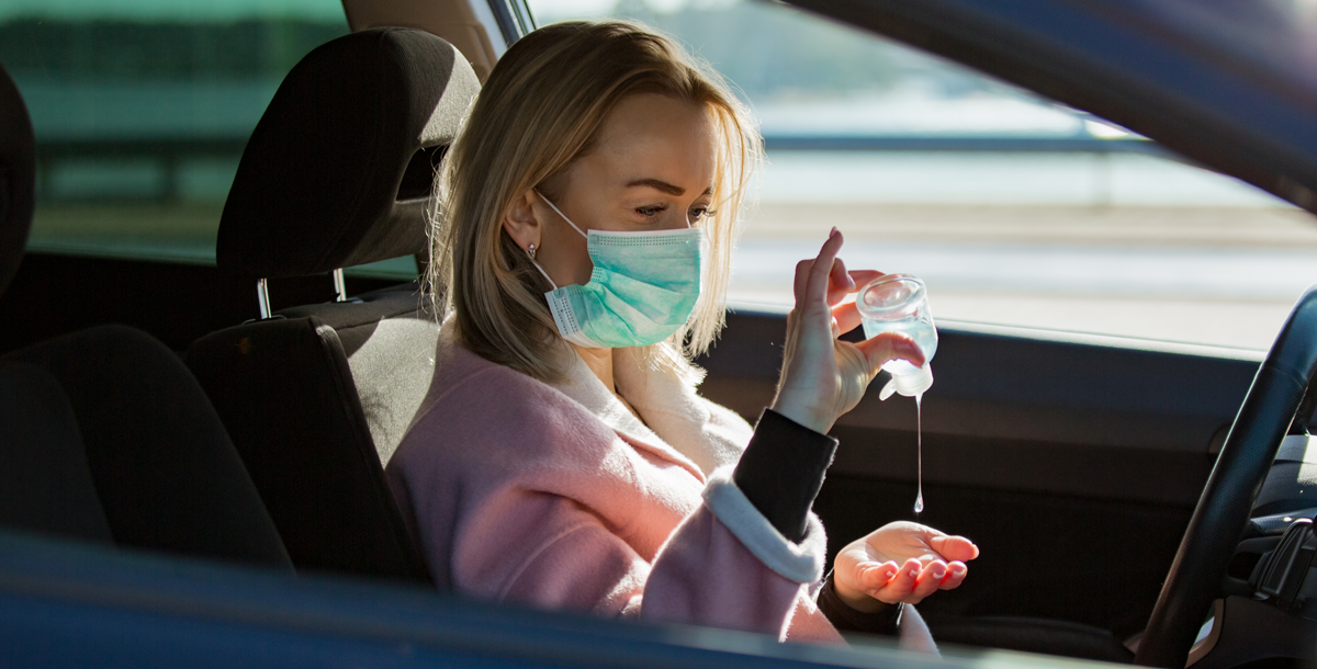 Woman using hand sanitizer in her care while wearing a face covering.