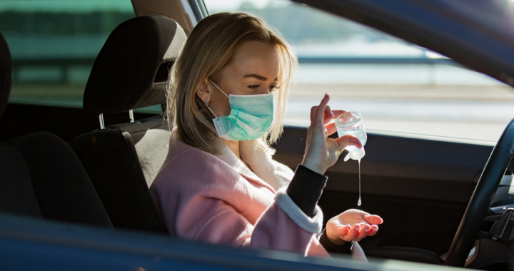 Woman using hand sanitizer in her care while wearing a face covering.