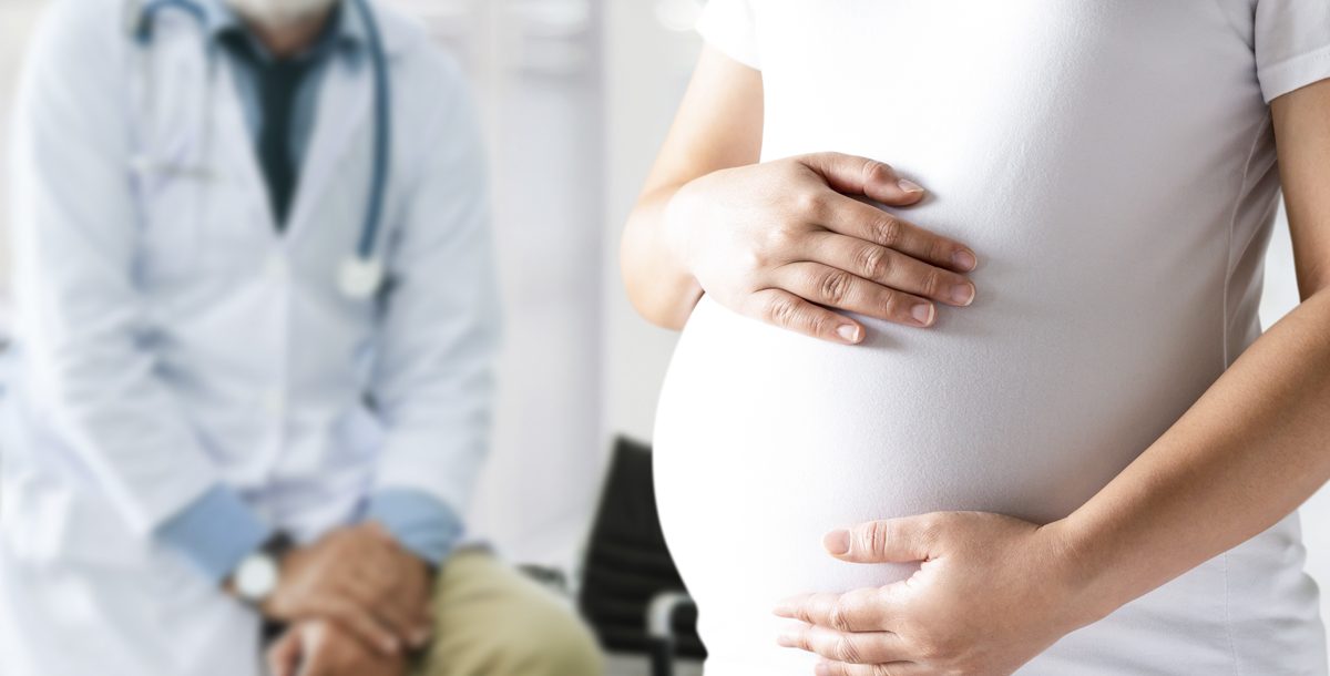 Pregnant women holding her baby bump with a physician in the background.