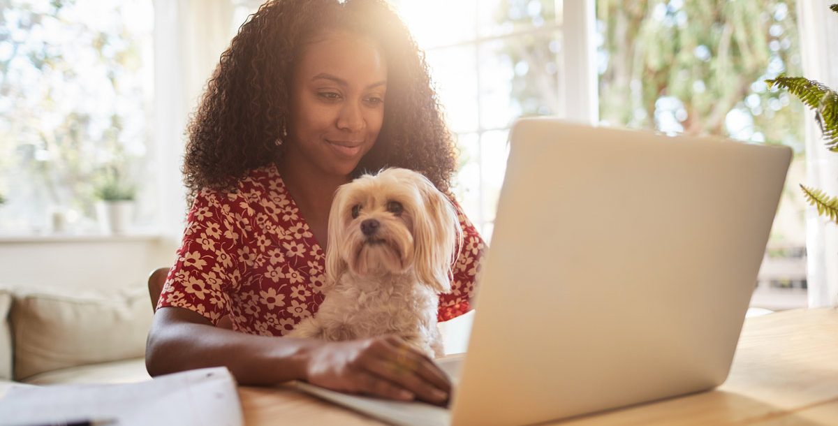 Woman working from home during COVID-19 with her dog on her lap.