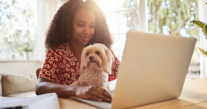 Woman working from home during COVID-19 with her dog on her lap.