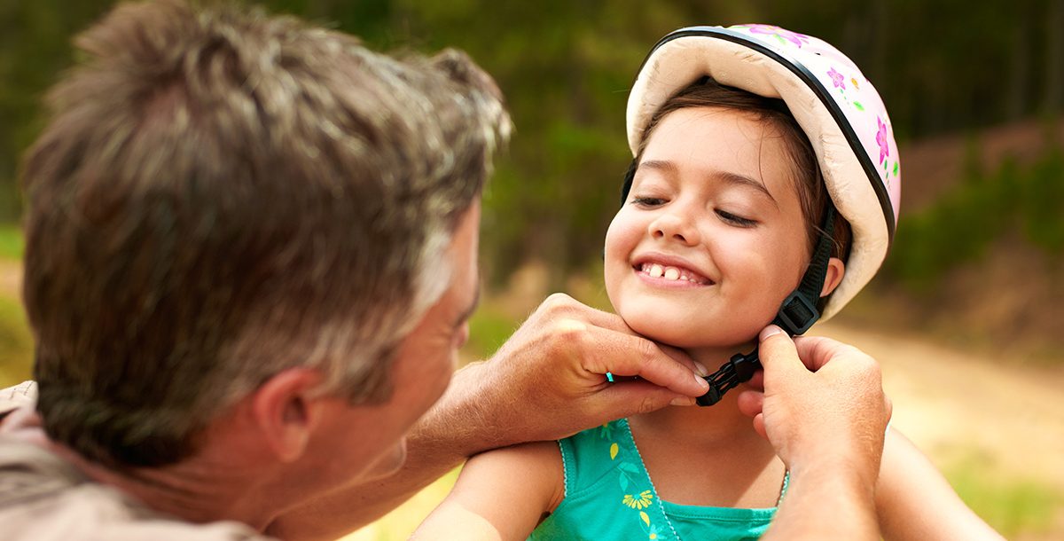 A dad helping is daughter put on her bike helmet.