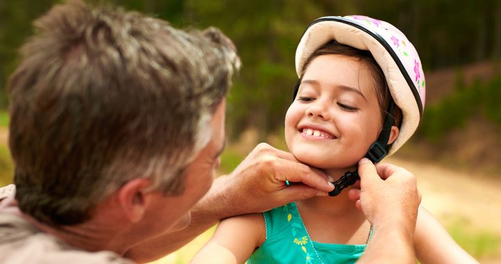 A dad helping is daughter put on her bike helmet.