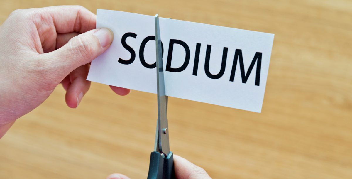 Scissors cutting the word "sodium" on a piece of paper.