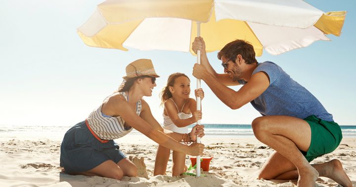 A family using an umbrella at the beach to protect themselves from the sun and UV rays.