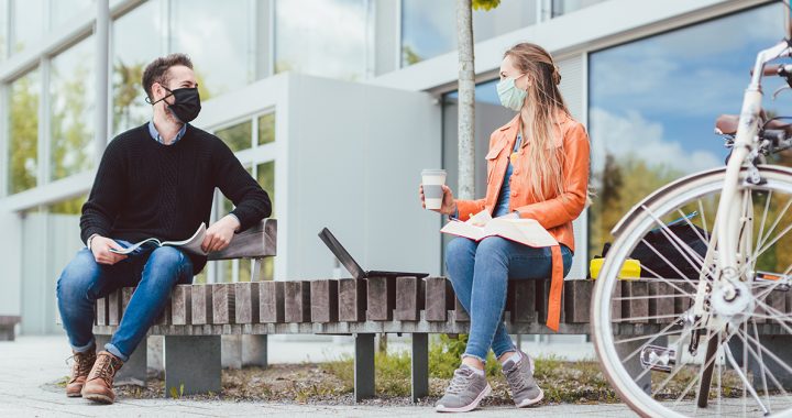 Two people wearing face masks in public while practicing social distancing.