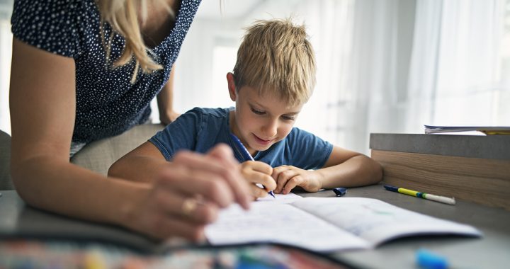 A young boy completing school at home with help from his mother.