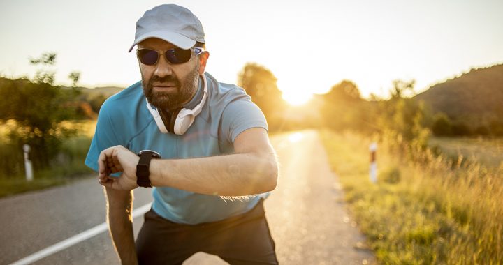 A man wearing sunglasses and a hat while running outside.