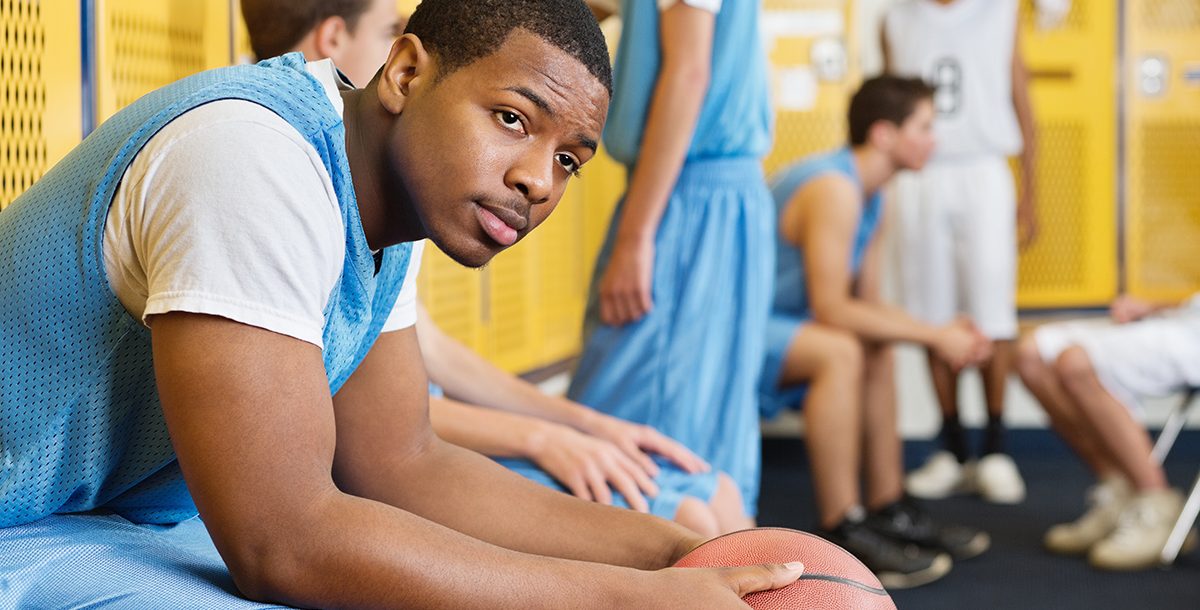 A high school athlete sitting in a locker room.